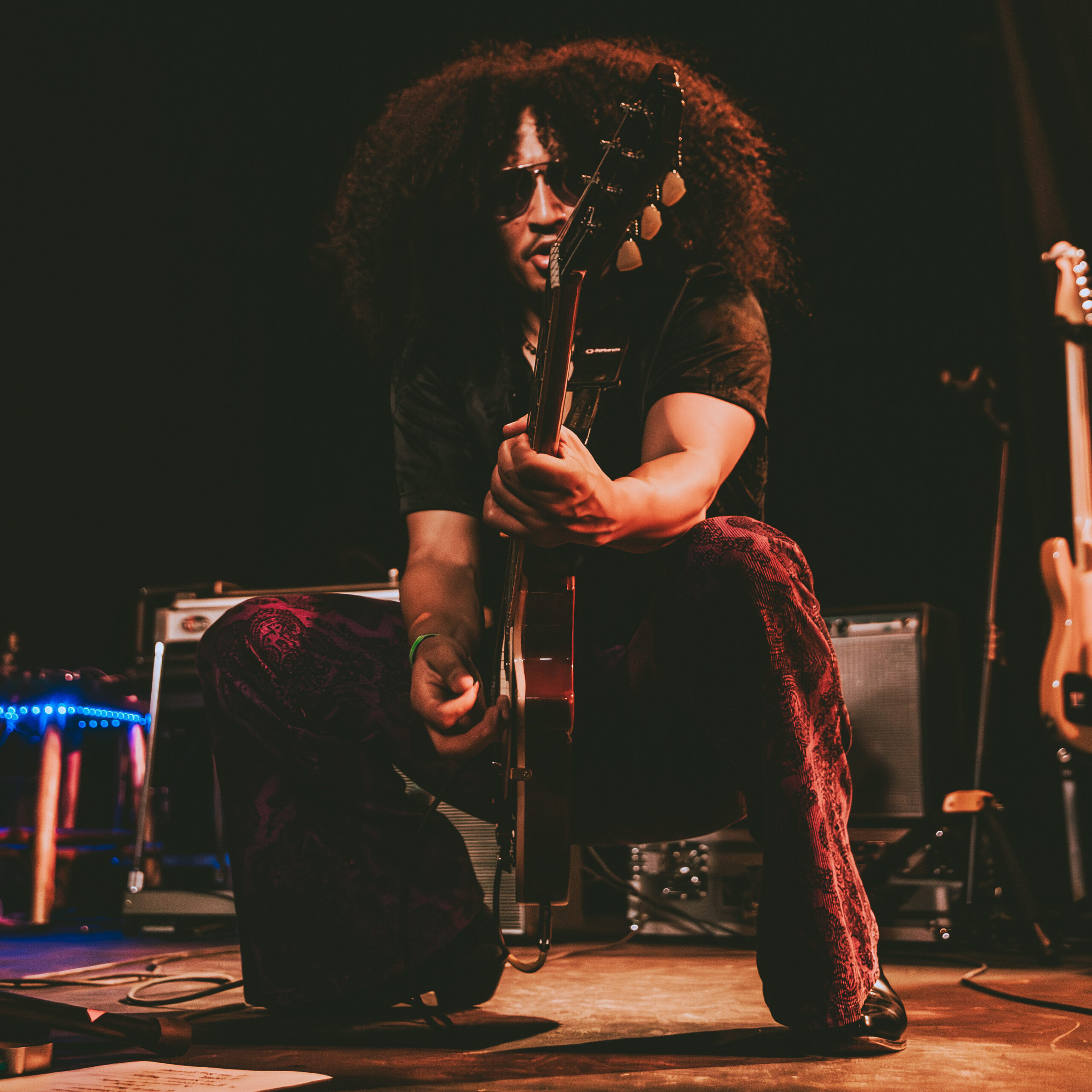 Tito is all grown up in this photo, and works the camera during a show at Amos' Southend in Charlotte, NC during a show with his band, Late Night Special. He poses mid-squat with his Les Paul guitar aimed at the camera between his legs, in a nod to legend Jimi Hendrix.